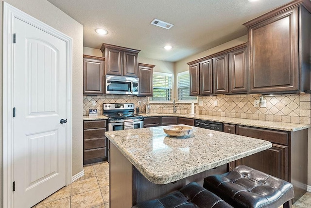 kitchen featuring appliances with stainless steel finishes, dark brown cabinetry, a kitchen bar, a sink, and tasteful backsplash