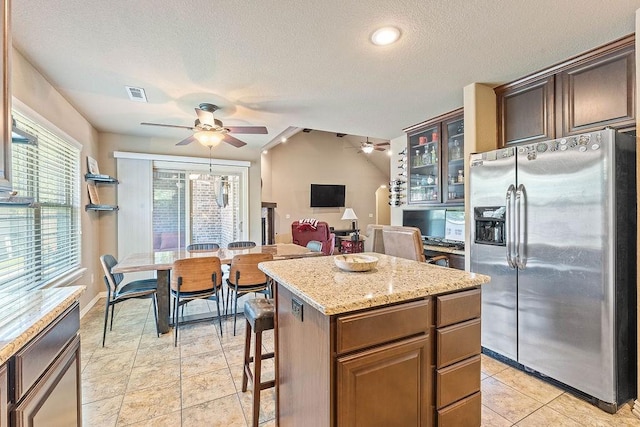 kitchen featuring stainless steel fridge, a ceiling fan, a center island, a textured ceiling, and glass insert cabinets