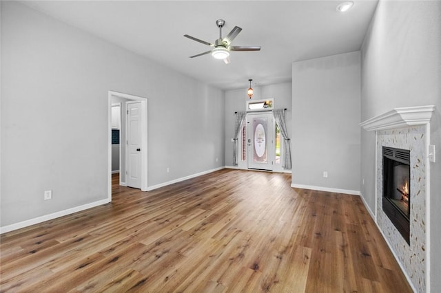 unfurnished living room featuring a ceiling fan, a glass covered fireplace, wood finished floors, and baseboards
