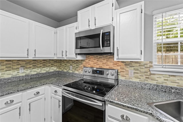 kitchen featuring appliances with stainless steel finishes, white cabinets, tasteful backsplash, and dark stone countertops