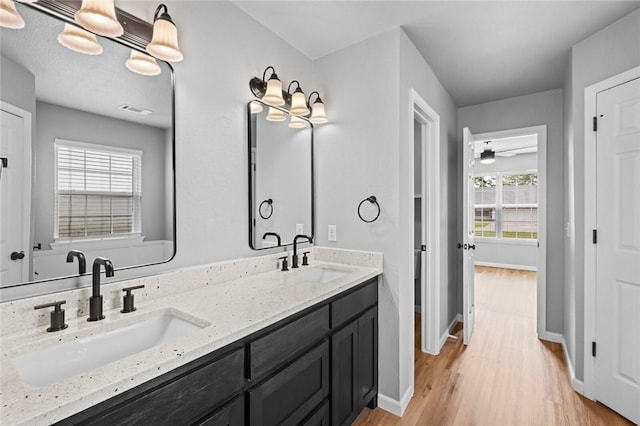 full bathroom with wood finished floors, baseboards, double vanity, and a ceiling fan