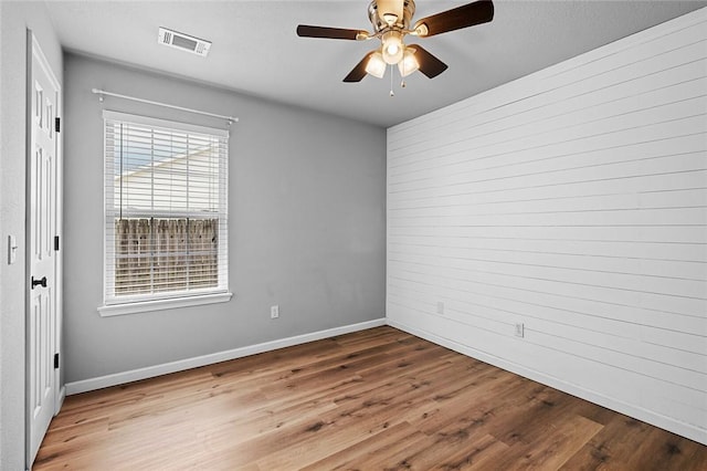 empty room with wood finished floors, a ceiling fan, baseboards, and wooden walls