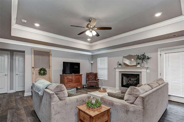 living room featuring a raised ceiling, ceiling fan, dark wood-type flooring, a fireplace, and crown molding