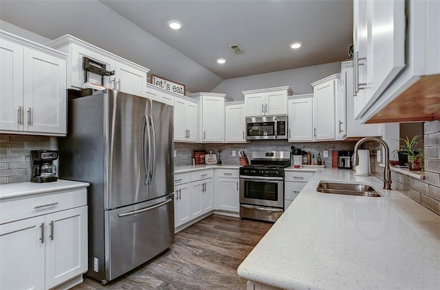 kitchen with appliances with stainless steel finishes, a sink, backsplash, white cabinetry, and vaulted ceiling