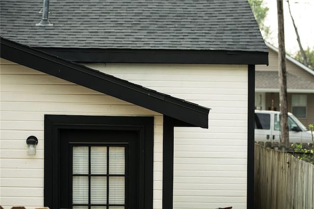 view of side of home featuring roof with shingles and fence