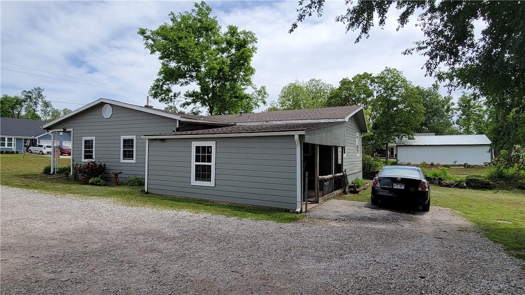 view of side of home with roof with shingles, gravel driveway, and a yard