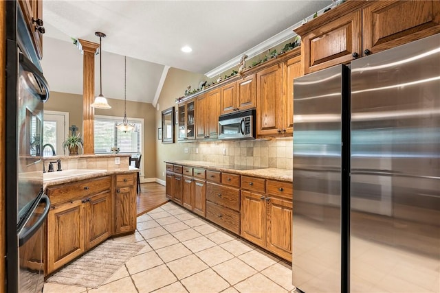 kitchen featuring stainless steel appliances, brown cabinets, backsplash, vaulted ceiling, and a sink