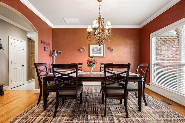 dining area with arched walkways, light wood-type flooring, a chandelier, crown molding, and baseboards