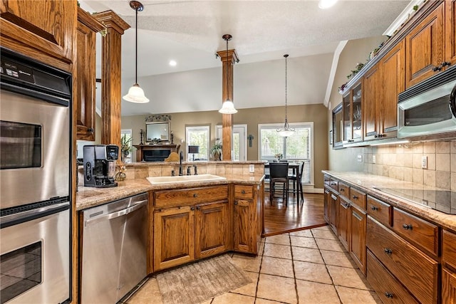 kitchen featuring appliances with stainless steel finishes, a sink, a peninsula, tasteful backsplash, and brown cabinetry