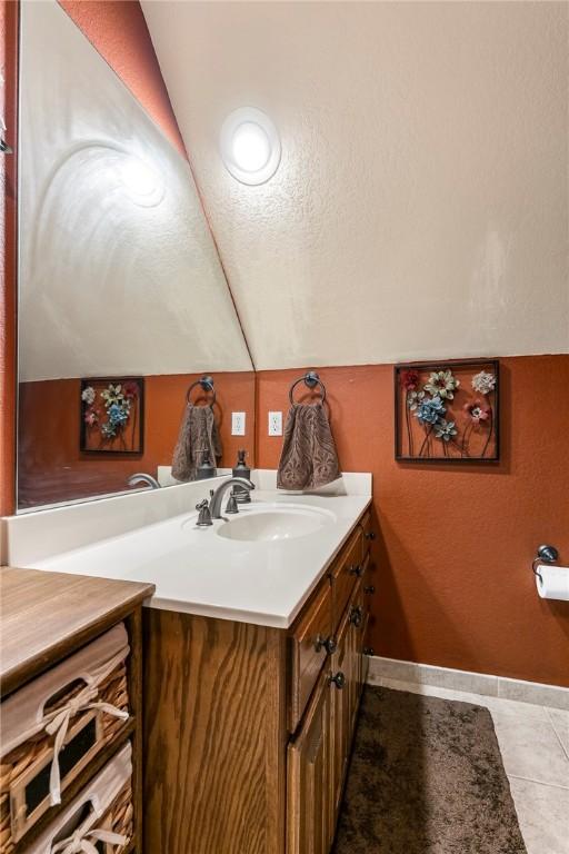 bathroom featuring lofted ceiling, vanity, baseboards, and tile patterned floors