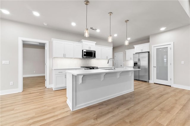 kitchen with stainless steel appliances, a sink, white cabinets, a center island with sink, and recessed lighting