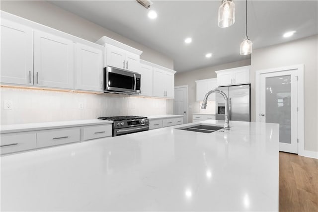 kitchen featuring appliances with stainless steel finishes, a sink, backsplash, decorative light fixtures, and white cabinetry