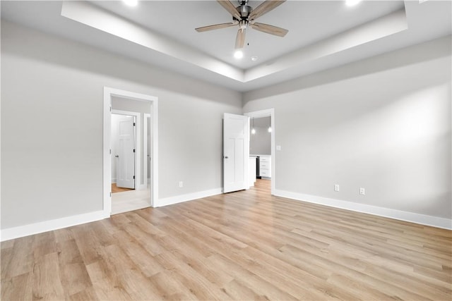 unfurnished bedroom featuring a raised ceiling, baseboards, recessed lighting, light wood-style flooring, and a ceiling fan