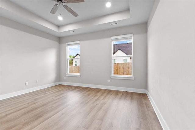unfurnished room featuring a tray ceiling, light wood-style floors, baseboards, a ceiling fan, and recessed lighting