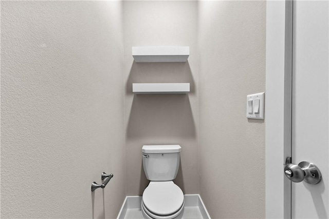 bathroom featuring baseboards, toilet, and a textured wall