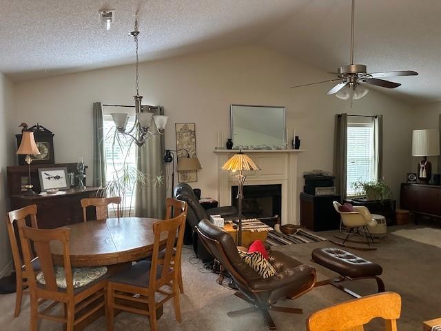 carpeted dining space with lofted ceiling, ceiling fan, a fireplace, and a textured ceiling