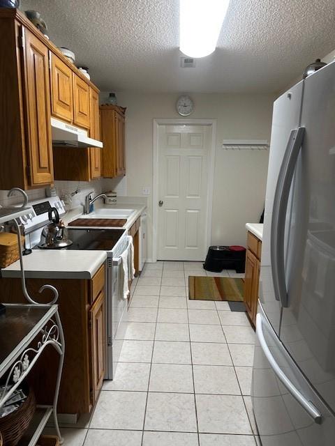 kitchen with freestanding refrigerator, electric range, under cabinet range hood, a sink, and a textured ceiling