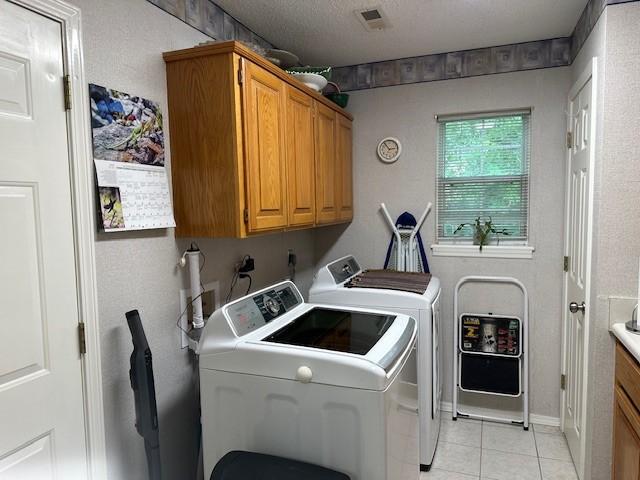 clothes washing area featuring independent washer and dryer, light tile patterned floors, and cabinet space