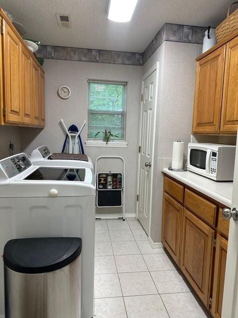 laundry area with washing machine and clothes dryer, light tile patterned floors, cabinet space, and a textured ceiling
