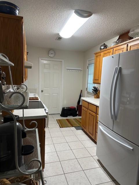 kitchen with freestanding refrigerator, a textured ceiling, light tile patterned flooring, light countertops, and under cabinet range hood