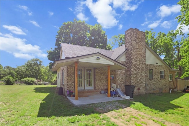 rear view of house with french doors, a yard, a chimney, brick siding, and a patio area