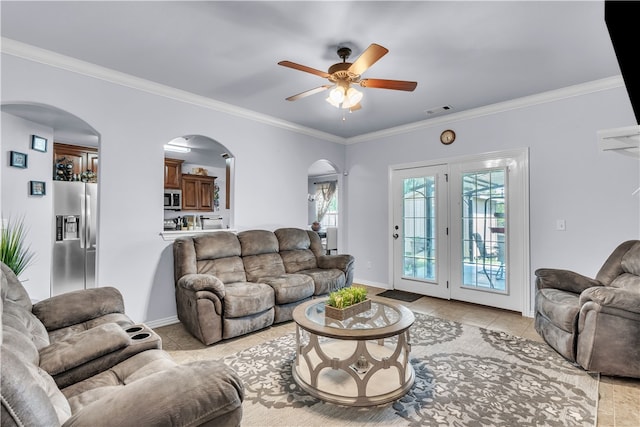 living area featuring arched walkways, ceiling fan, light tile patterned floors, crown molding, and baseboards