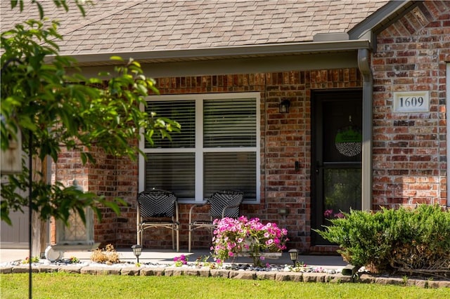 view of exterior entry featuring brick siding and roof with shingles