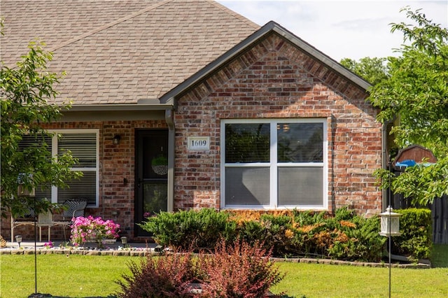view of front of house with brick siding, a front yard, and a shingled roof