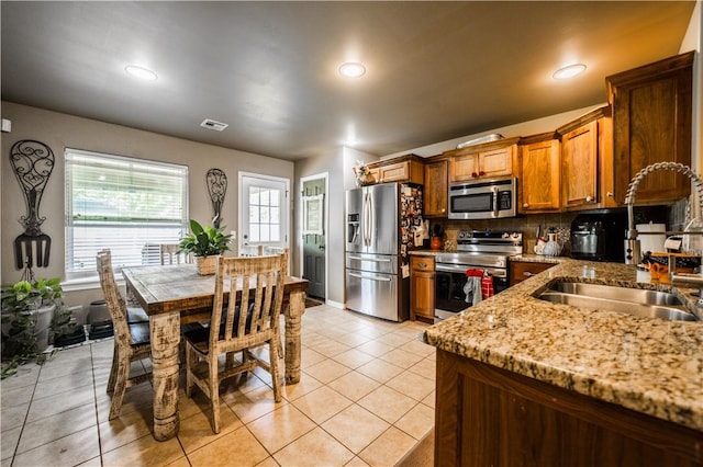kitchen with stainless steel appliances, a sink, brown cabinetry, backsplash, and light tile patterned flooring