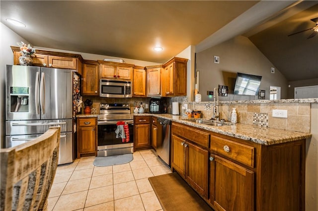 kitchen featuring appliances with stainless steel finishes, a sink, a peninsula, decorative backsplash, and brown cabinetry