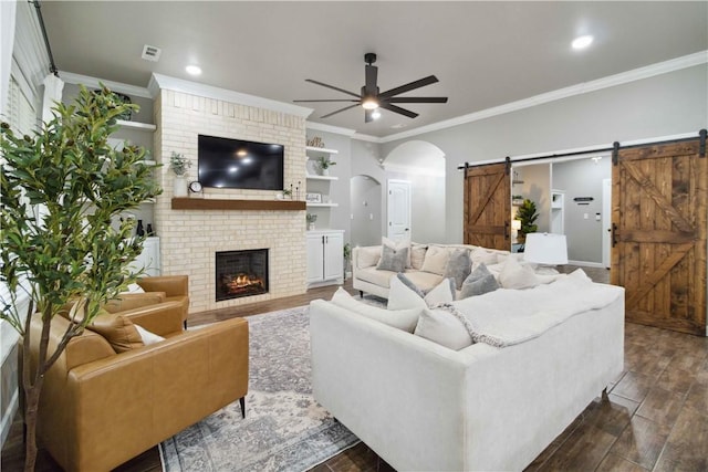 1904 Tull Dr, Pea Ridge, AR 72751 - living room featuring a barn door, ceiling fan, arched walkways, dark wood-style flooring, and ornamental molding
