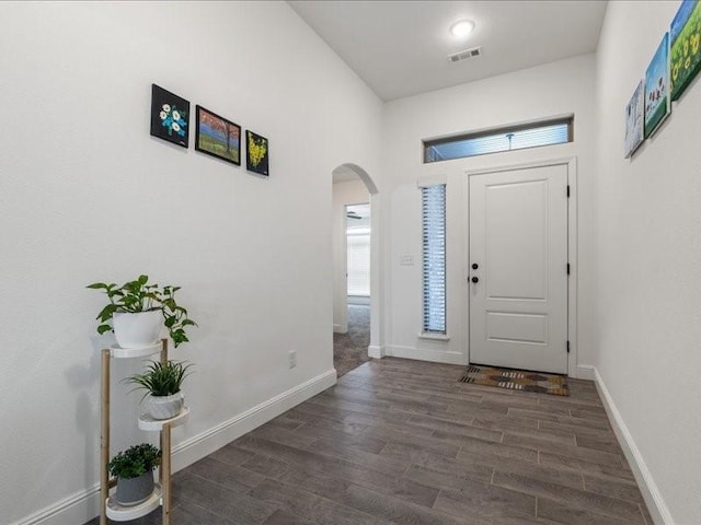 foyer featuring arched walkways, wood finished floors, and baseboards