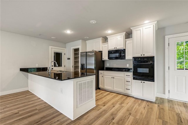 kitchen with black appliances, a sink, white cabinets, light wood-style floors, and a peninsula