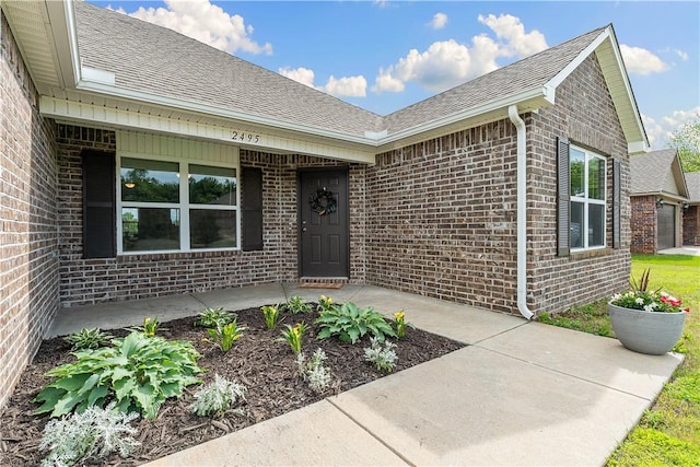 view of exterior entry featuring brick siding, a shingled roof, and covered porch