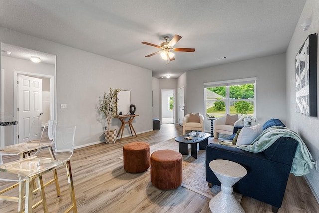 living room featuring light wood finished floors, a ceiling fan, and baseboards