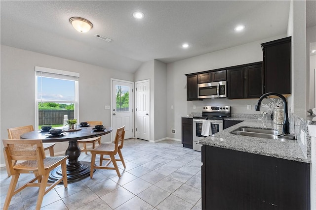 kitchen featuring appliances with stainless steel finishes, a sink, light stone counters, vaulted ceiling, and baseboards