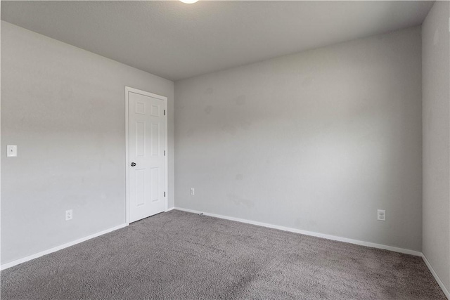 empty room featuring dark colored carpet and baseboards