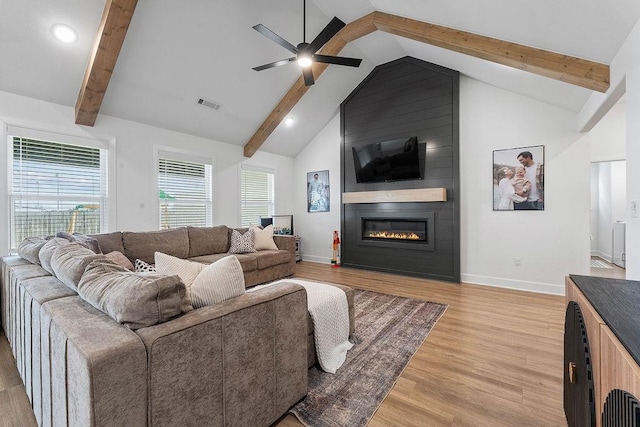 living area with beamed ceiling, light wood finished floors, ceiling fan, baseboards, and a large fireplace