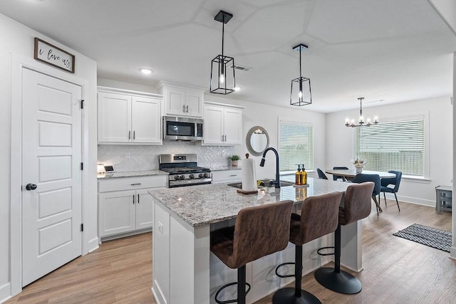 kitchen with appliances with stainless steel finishes, a sink, light wood-type flooring, a center island with sink, and light stone countertops