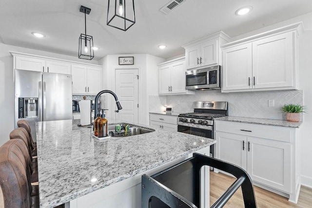 kitchen with appliances with stainless steel finishes, a sink, a kitchen breakfast bar, white cabinetry, and recessed lighting