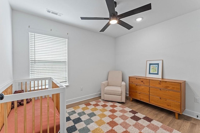 bedroom featuring wood finished floors, recessed lighting, baseboards, a crib, and ceiling fan