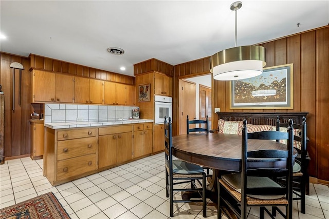 kitchen with oven, wood walls, tile counters, light tile patterned floors, and brown cabinets