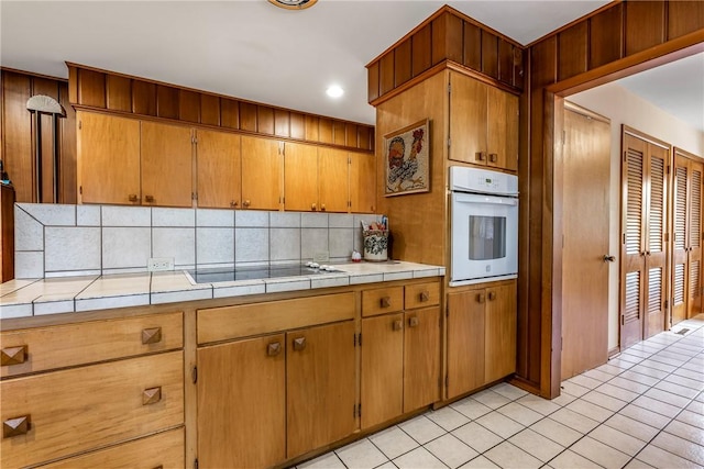 kitchen with white oven, backsplash, tile countertops, black electric stovetop, and recessed lighting
