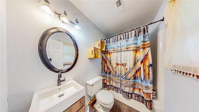 full bath featuring toilet, vanity, wood finished floors, and a textured wall