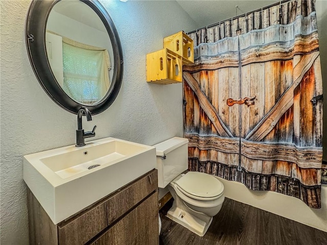 full bath featuring a textured wall, wood finished floors, toilet, vanity, and a shower with curtain