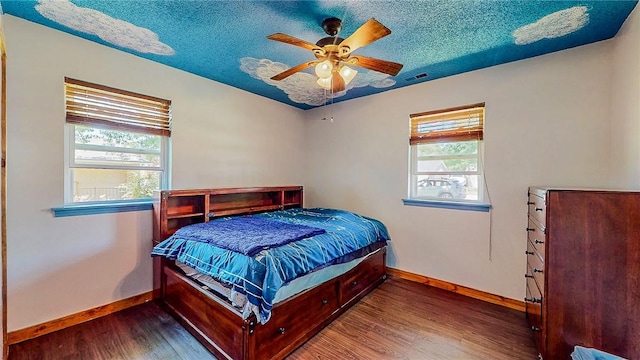 bedroom featuring baseboards, multiple windows, wood finished floors, a textured ceiling, and ceiling fan