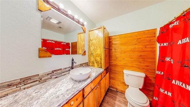 bathroom with a textured wall, wood finished floors, toilet, vanity, and a textured ceiling