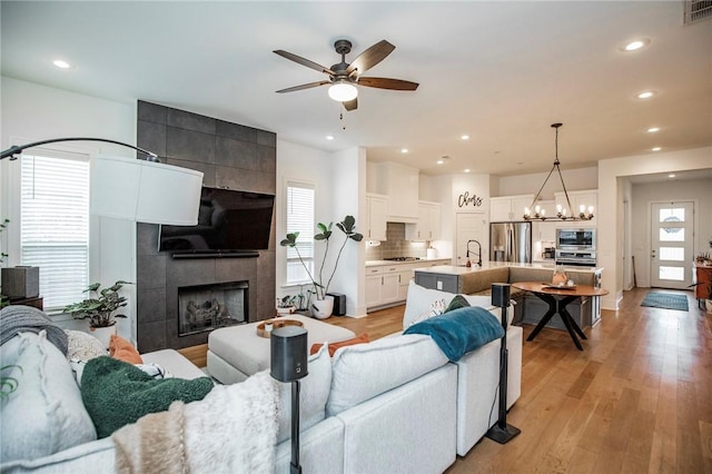 living area featuring ceiling fan, a chandelier, recessed lighting, a tile fireplace, and light wood-style flooring