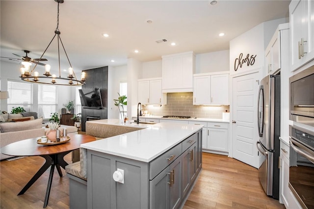 kitchen with stainless steel appliances, gray cabinets, a sink, open floor plan, and backsplash