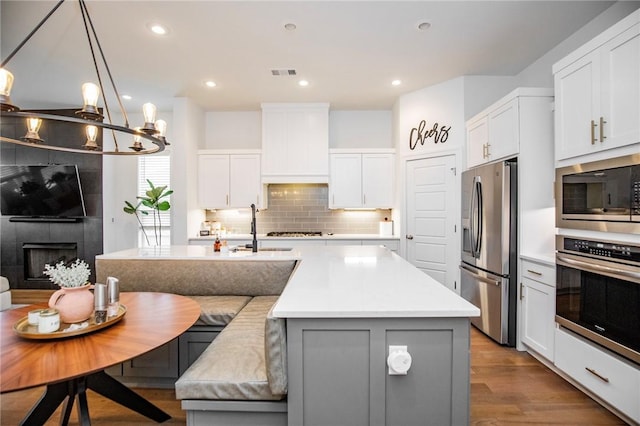 kitchen featuring appliances with stainless steel finishes, a sink, backsplash, light countertops, and a center island with sink